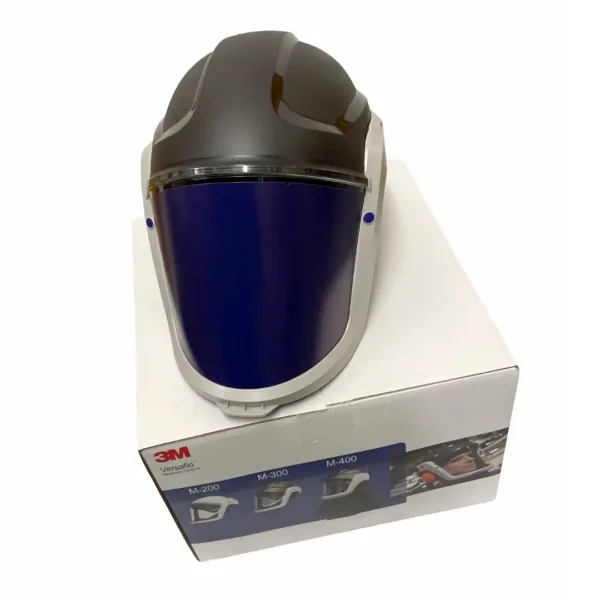 3M Versaflo M-306 Helmet – Top view of the protective helmet placed on its original packaging. Features an integrated face shield with a large visor for clear visibility, lightweight construction, and a durable design for industrial use.